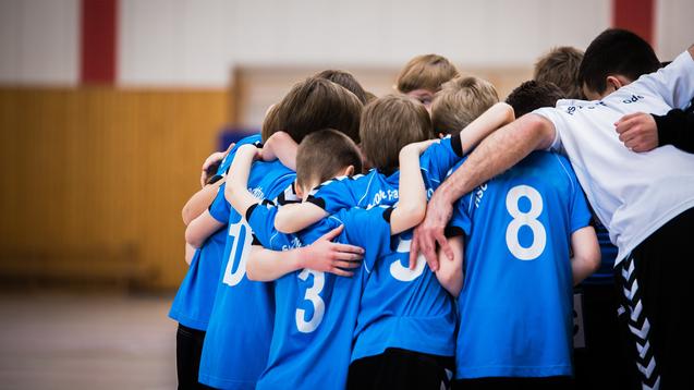 Gruppe junger Sportler in blauen Trikots umarmt sich in einer Halle vor dem Spiel.